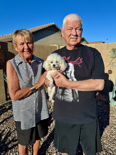 Two adults standing in a backyard with a small white dog, showing Meka with her family as she learns to feel safe and understood.